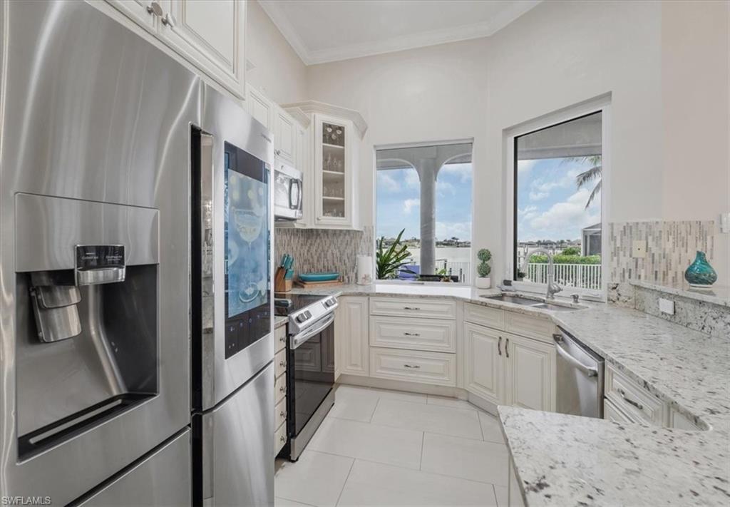 Kitchen featuring appliances with stainless steel finishes, light stone countertops, glass insert cabinets, tasteful backsplash, and crown molding