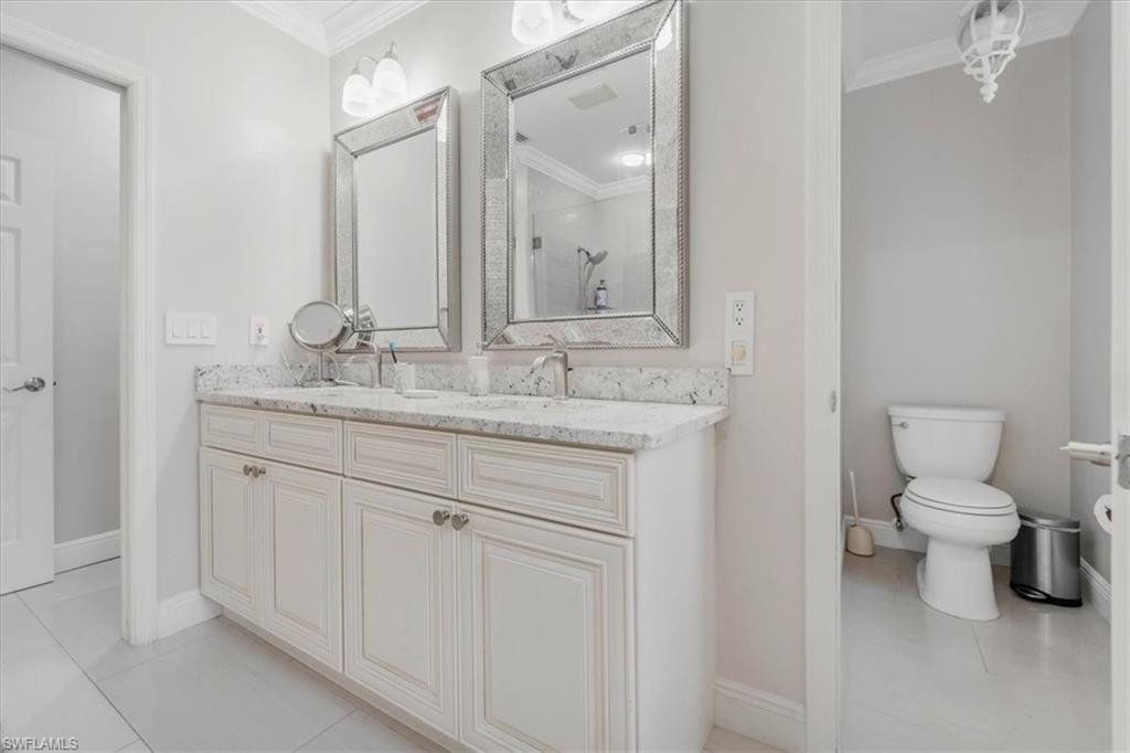 Full bath featuring light tile patterned flooring, ornamental molding, double vanity, and a stall shower