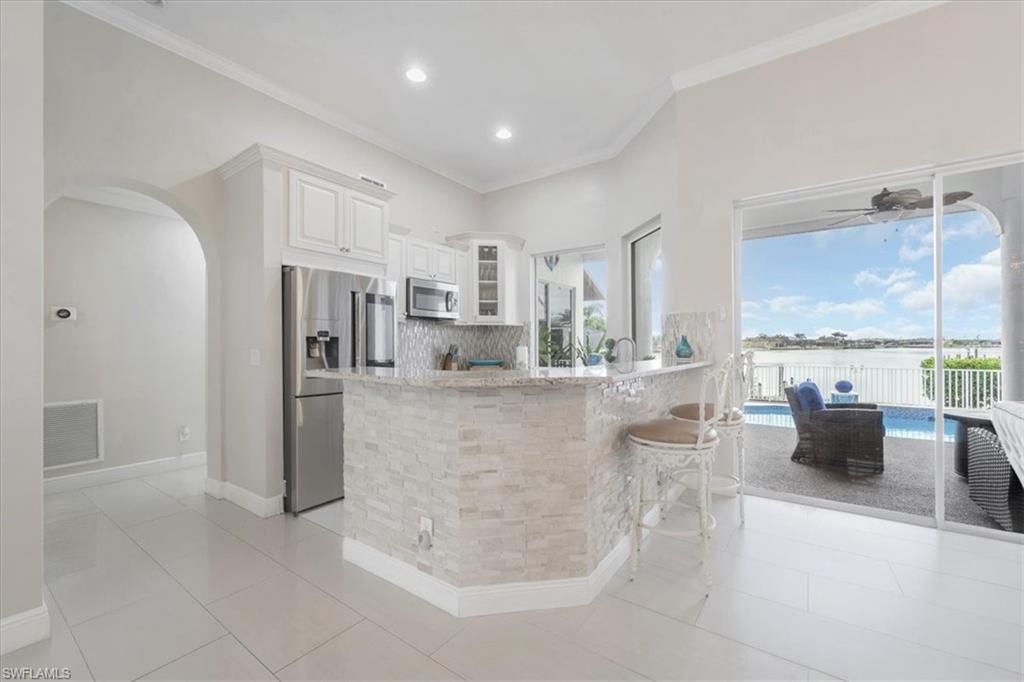 Kitchen featuring glass insert cabinets, tasteful backsplash, stainless steel appliances, white cabinets, and light stone counters