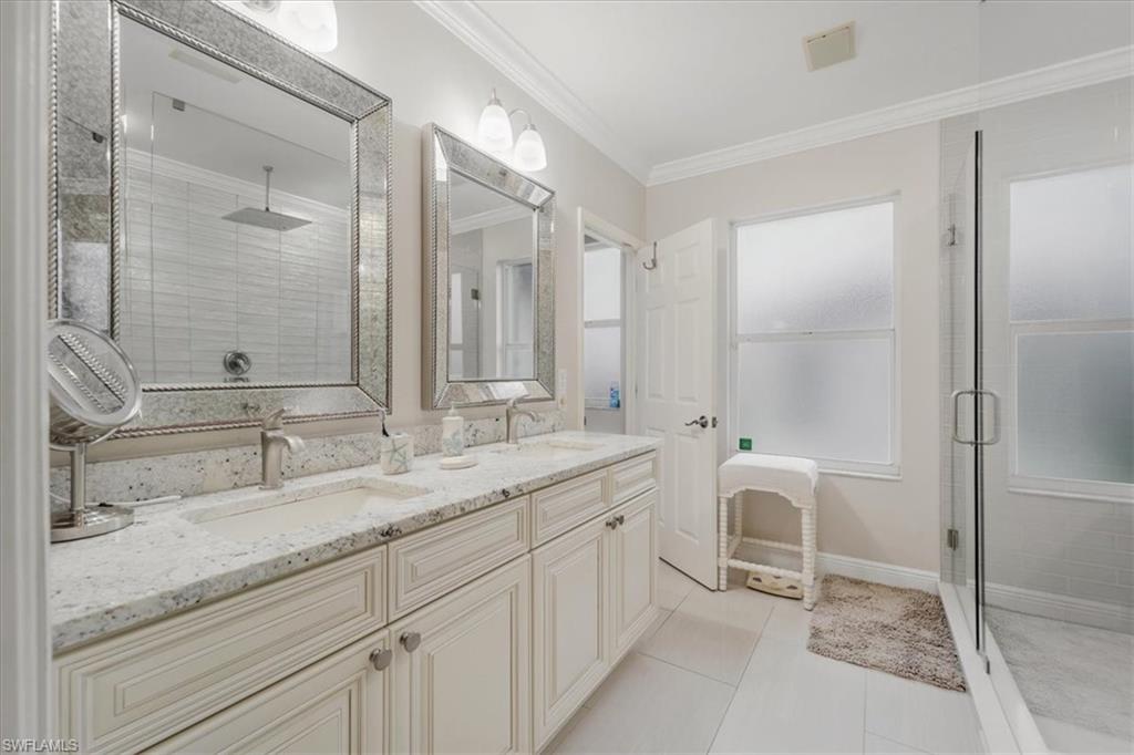 Full bathroom featuring a stall shower, double vanity, crown molding, and light tile patterned floors