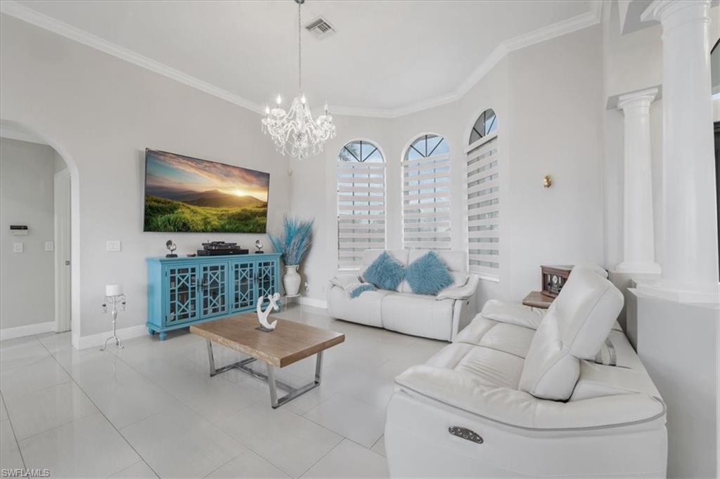 Living area with arched walkways, ornamental molding, tile patterned floors, and a chandelier