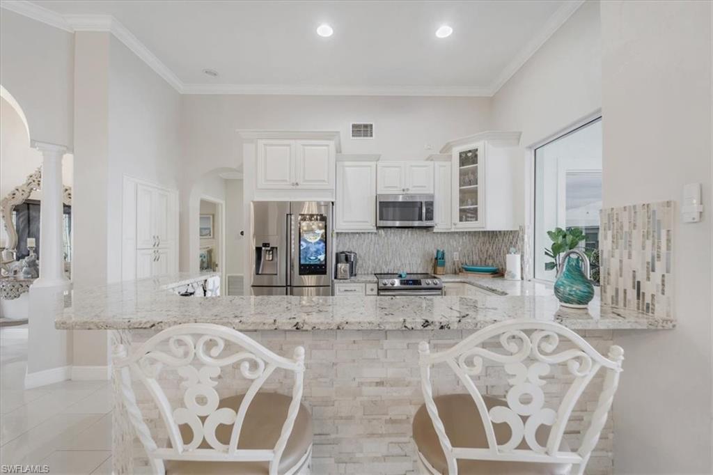 Kitchen featuring a breakfast bar area, ornamental molding, light stone countertops, glass insert cabinets, and decorative backsplash