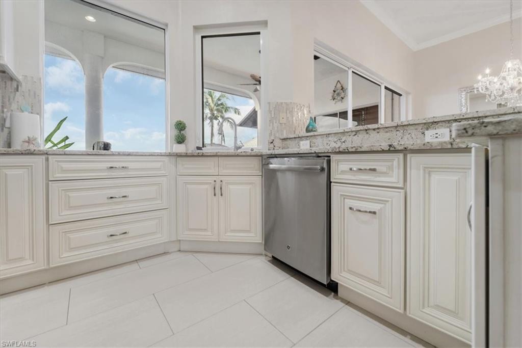 Kitchen with light tile patterned floors, light stone counters, dishwasher, a chandelier, and decorative light fixtures