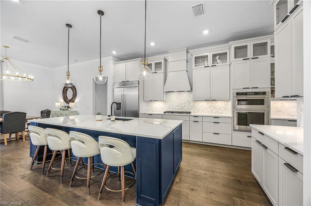 Dual tone kitchen with a breakfast bar, a kitchen island with sink, dark wood finished floors, backsplash, and ornamental molding