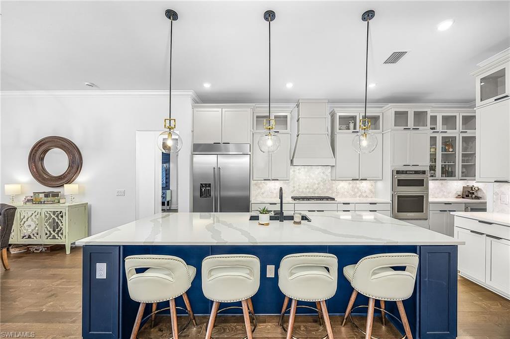 Two tone kitchen featuring dual tone cabinets, a spacious island, tasteful backsplash, glass fronted cabinets, and a breakfast bar area