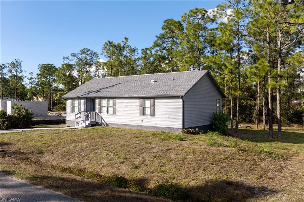 View of front of property with a front lawn, roof with shingles, and view of wooded area
