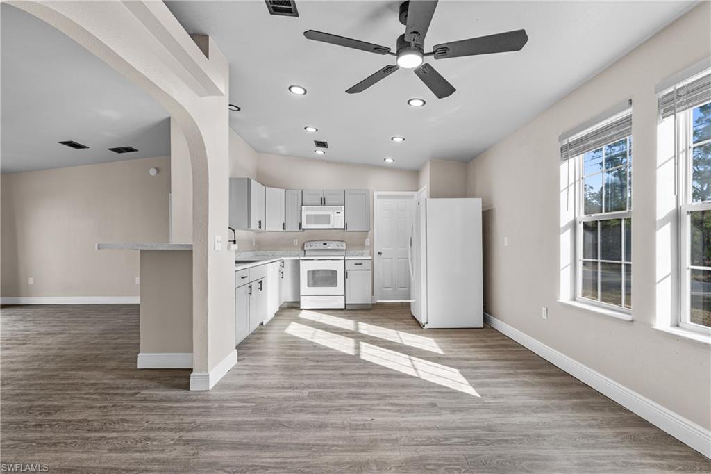 Kitchen with light countertops, white appliances, arched walkways, open floor plan, and light wood-type flooring