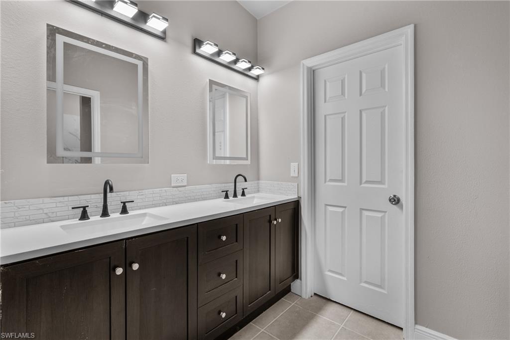 Bathroom featuring double vanity, tasteful backsplash, and light tile patterned floors
