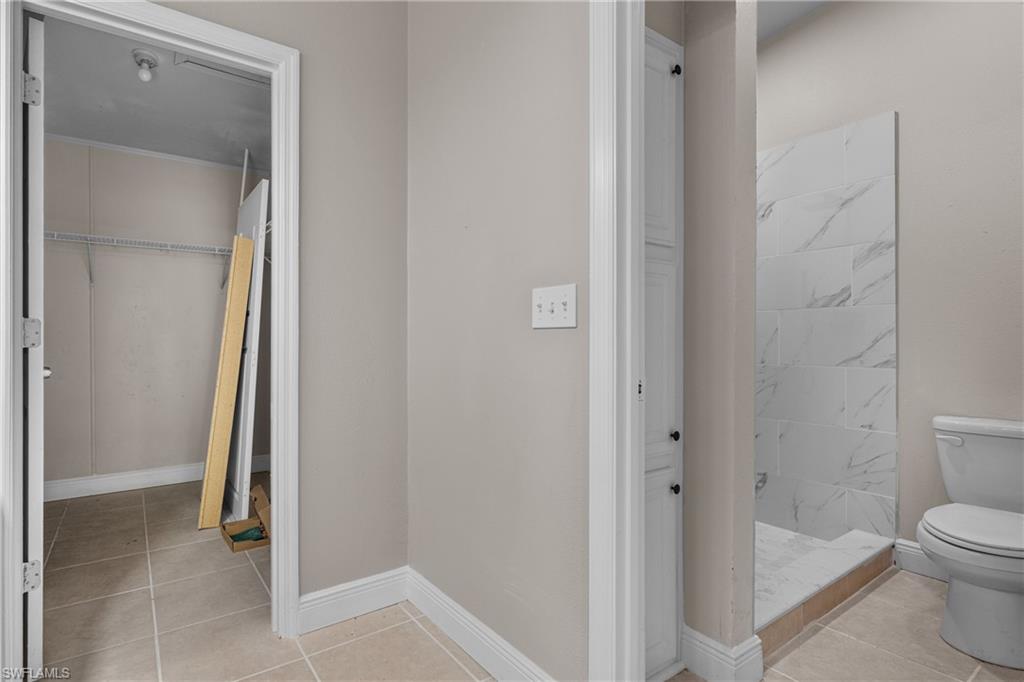 Full bath featuring a spacious closet, light tile patterned flooring, and a stall shower