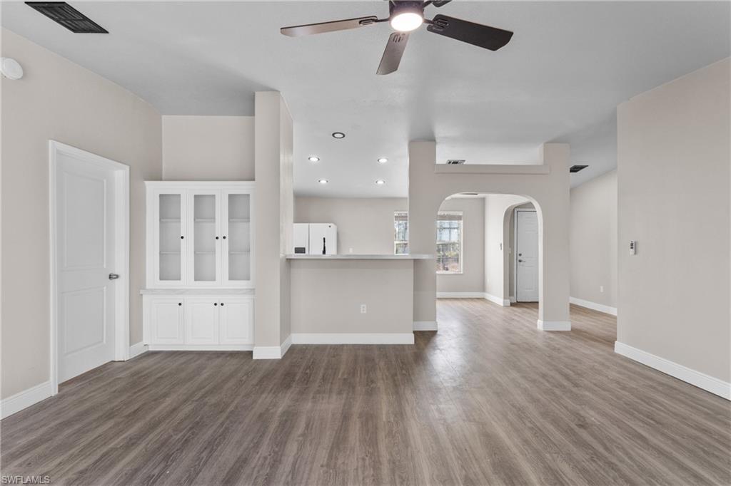 Unfurnished living room featuring arched walkways, dark wood-style flooring, ceiling fan, and recessed lighting