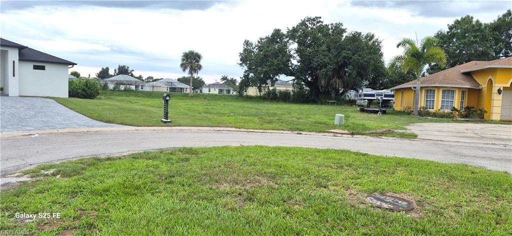 Expansive grass-covered lot featuring mature trees and a residential street frontage