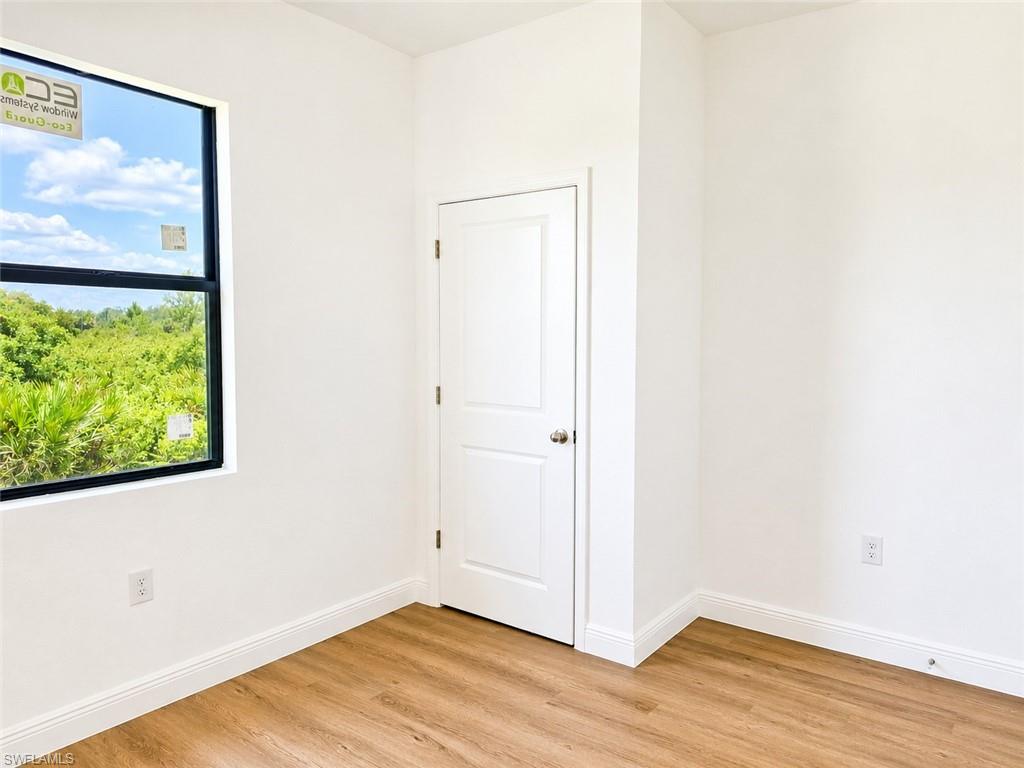 Bright interior space featuring a large window with black framing, wood-finish flooring, white baseboards, and a white two-panel door with a brushed nickel knob