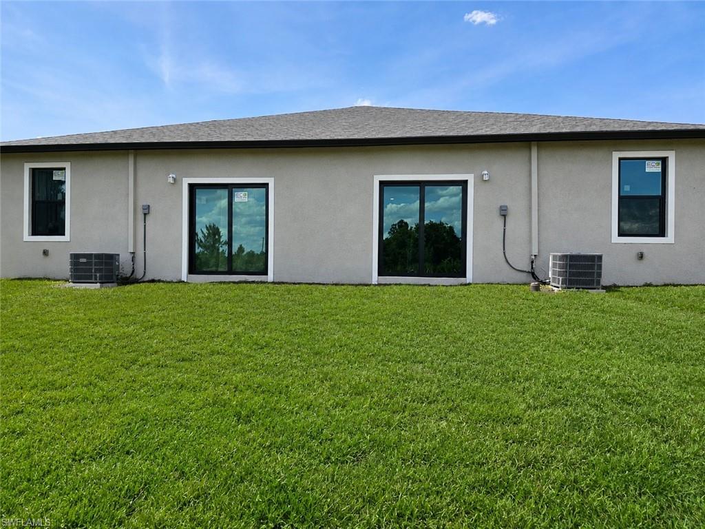 Rear exterior featuring a stucco finish, two sliding glass doors with black frames, two windows with white trim, and a shingle roof