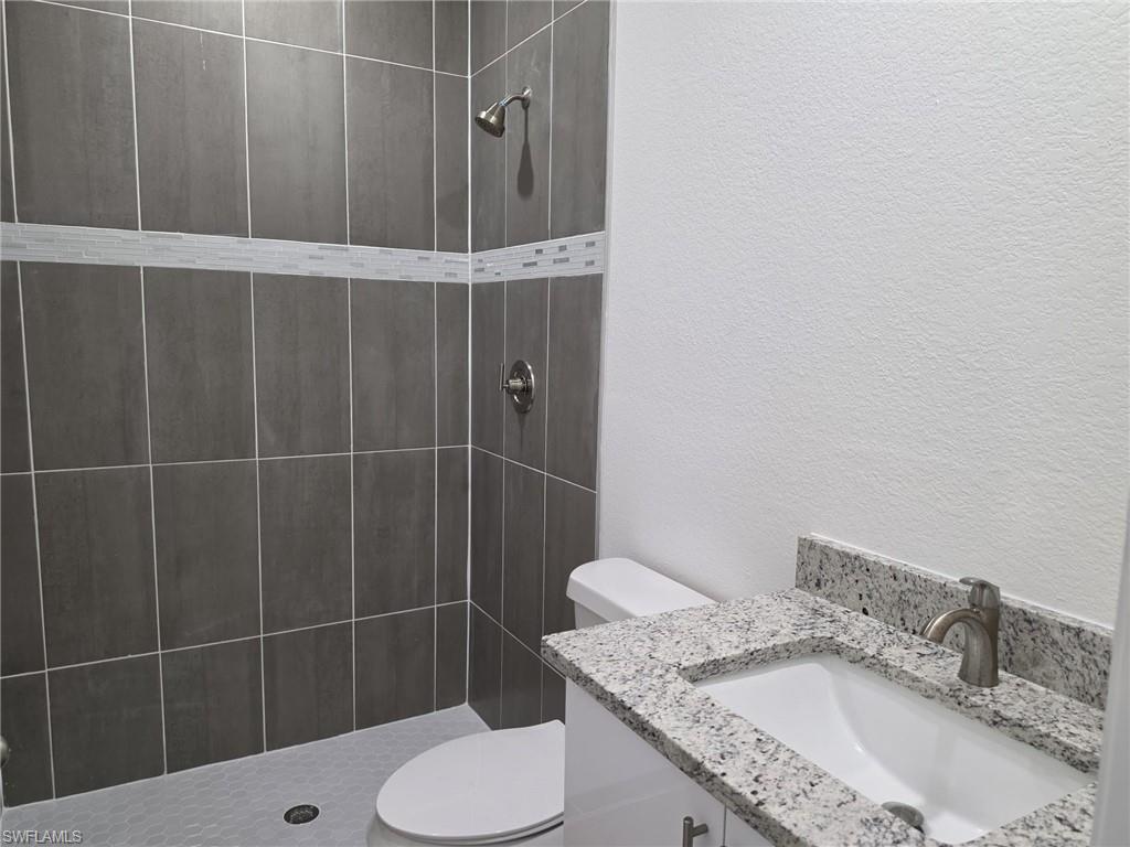 Bathroom featuring a walk-in shower with dark gray rectangular wall tiles, a decorative light-colored mosaic tile band, and a hexagonal floor tile