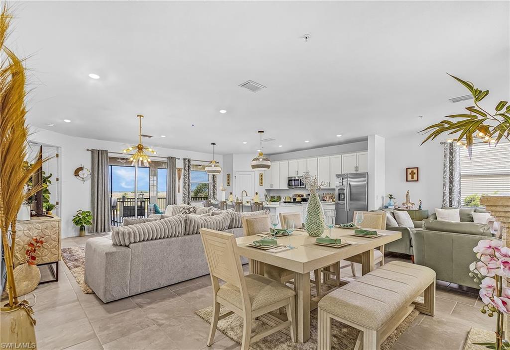 Open-concept living space featuring large format tile flooring, a dining area with a rectangular table and bench seating, and a kitchen with white cabinetry and stainless steel appliances