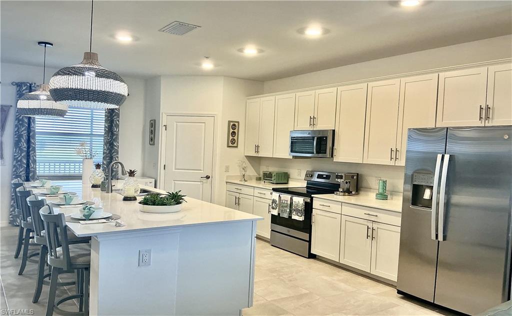 Kitchen featuring a large central island with seating for four, white shaker-style cabinetry, stainless steel appliances, recessed ceiling lighting, and light-toned tile flooring