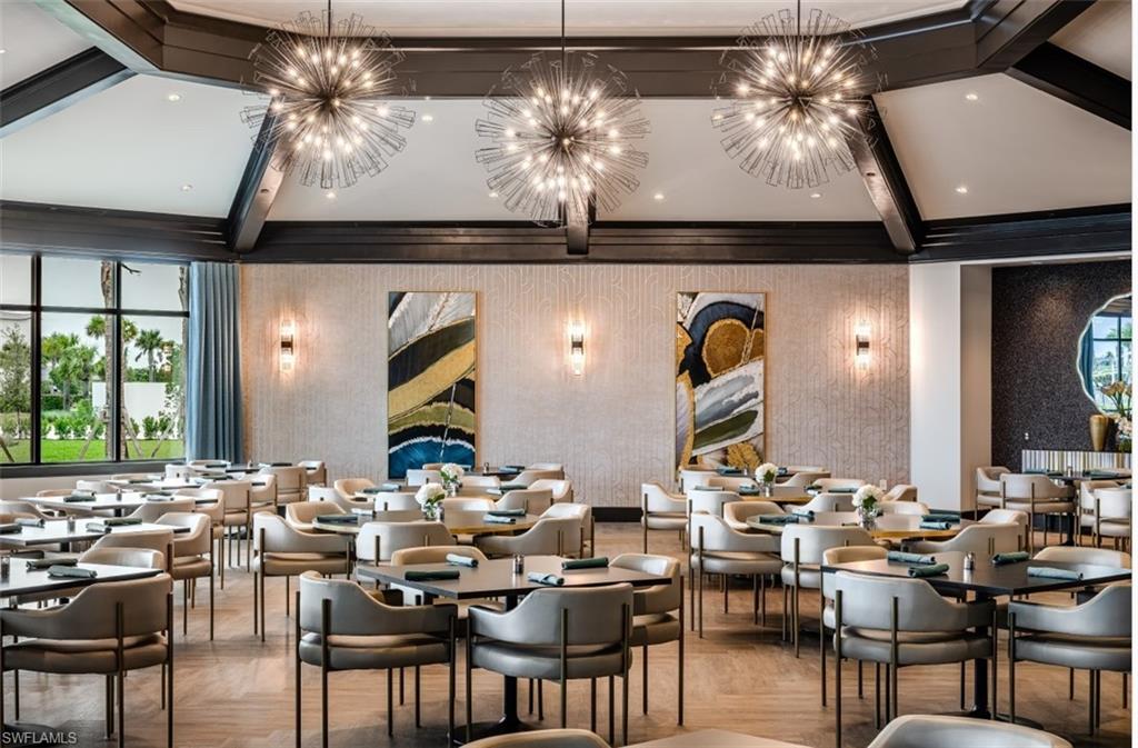 Spacious dining area featuring a vaulted ceiling with dark wood beams, three spherical chandeliers, a window wall with exterior landscaping, and wood-finish flooring