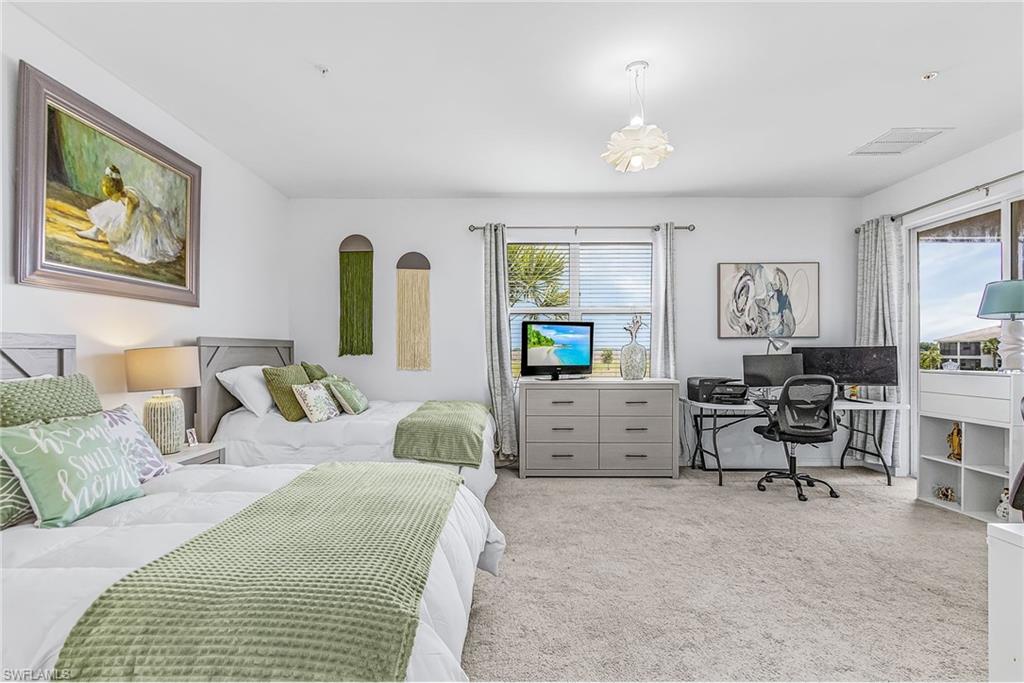 Spacious room featuring light gray carpet flooring, two beds with light gray wooden headboards, and a dedicated workspace with a desk and chair