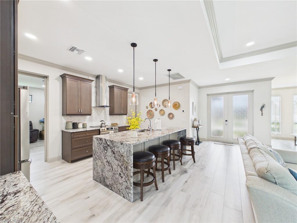 Open-concept kitchen featuring a large island with a waterfall countertop, pendant lighting, stainless steel appliances, and a tile backsplash