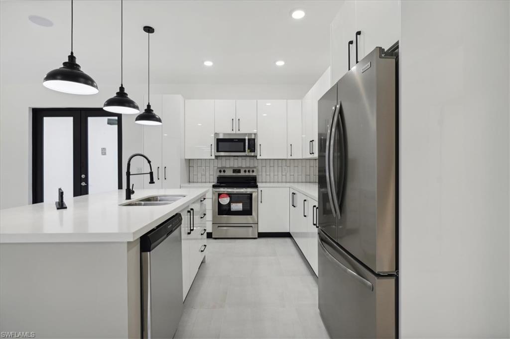 Kitchen with white cabinets, backsplash, hanging light fixtures, appliances with stainless steel finishes, and sink