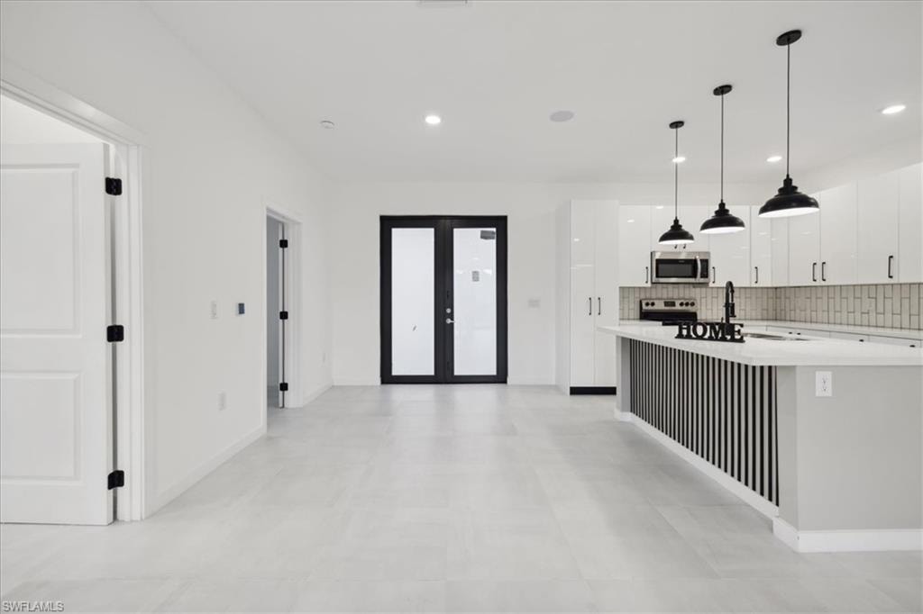 Kitchen with white cabinetry, decorative light fixtures, stainless steel appliances, decorative backsplash, and french doors