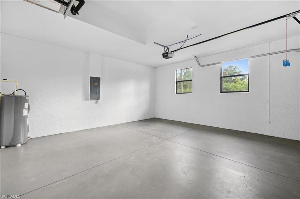 Garage featuring electric panel, electric water heater, and a garage door opener