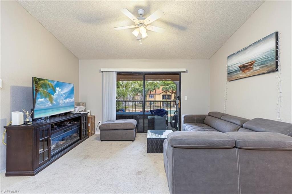 Living room with a textured ceiling, carpet flooring, and a ceiling fan