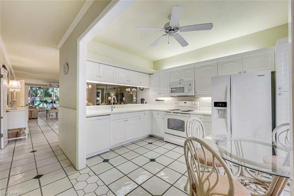 KITCHEN FEATURING WHITE GLOSS RAISED PROFILE CABINETS, WHITE CORIAN COUNTERS, WHITE APPLIANCES AND TILE FLOORS.