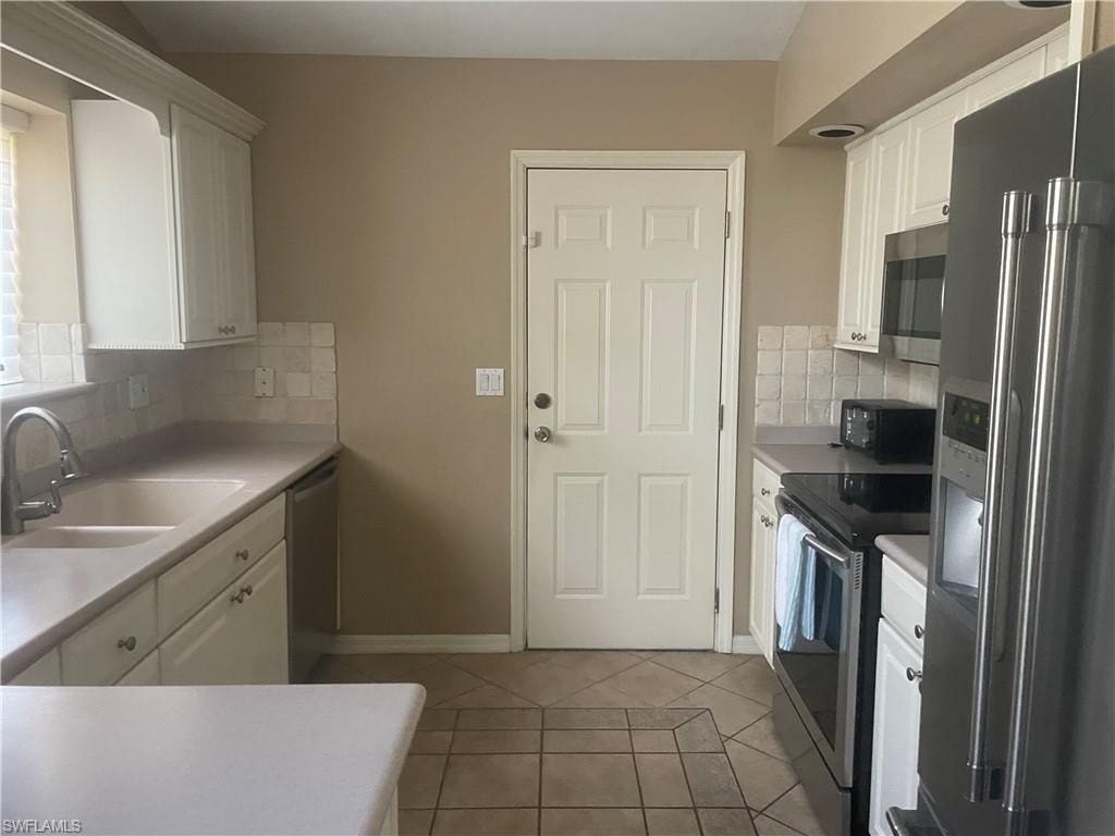 Kitchen featuring white cabinetry, light-toned countertops, a light-toned tile backsplash, and tile flooring