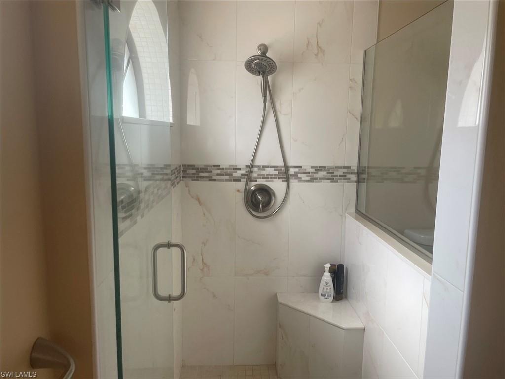 Glass-enclosed shower with white tiled walls, a decorative mosaic tile band, a built-in shower bench, and a brushed nickel shower fixture