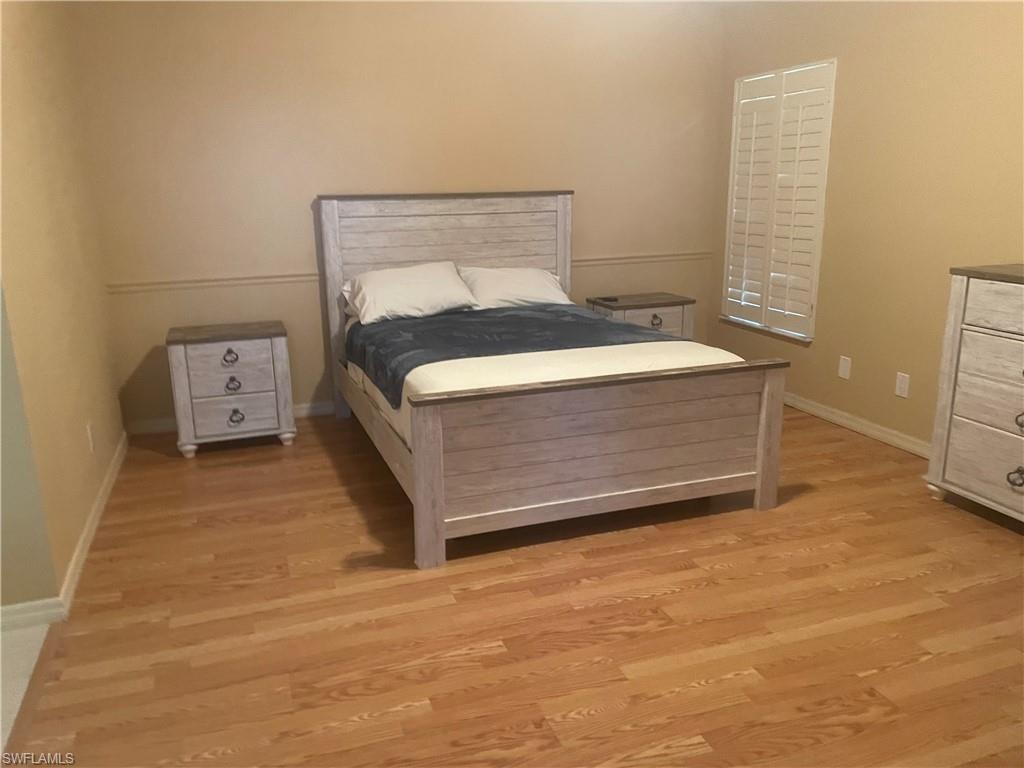 Spacious room featuring wood-finish flooring, neutral wall tones, and a window with plantation shutters