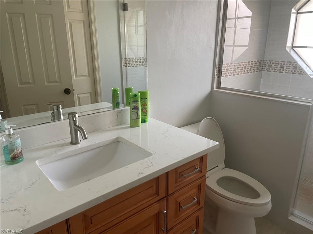 Bathroom featuring a wood-finish vanity with a white countertop and integrated sink, a brushed nickel faucet, an elongated toilet, a mirror, and a window with privacy glass