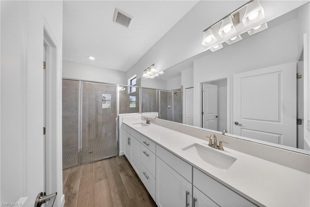 Bathroom featuring a dual vanity with white cabinetry and integrated sinks, a large wall-mounted mirror, and overhead lighting fixtures