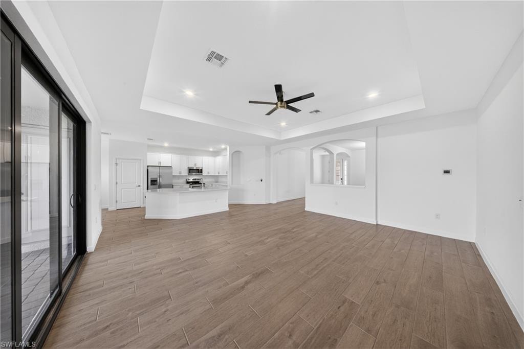 Expansive living area featuring wood-finish tile flooring and a tray ceiling with recessed lighting and a ceiling fan