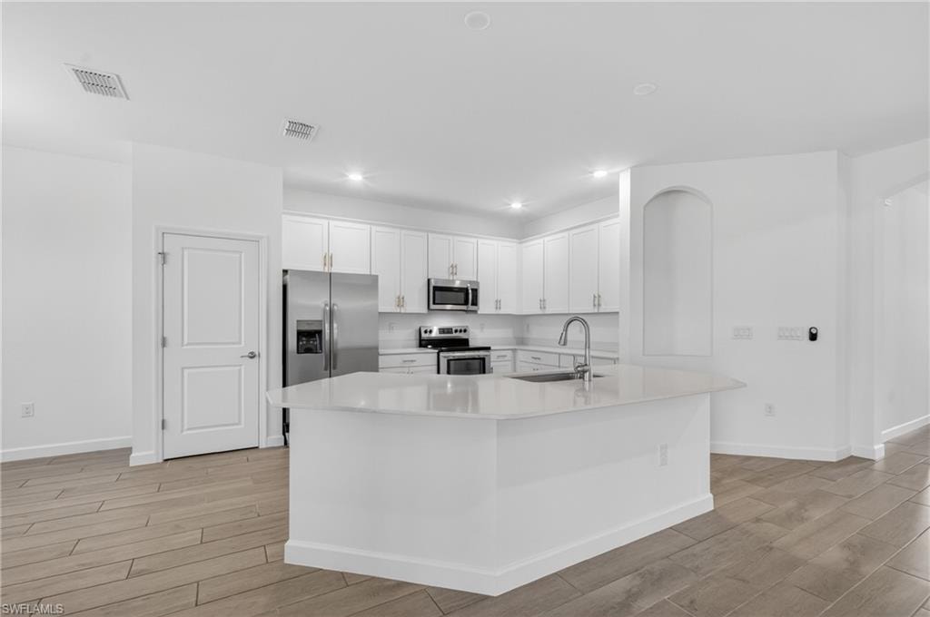 Modern kitchen featuring white cabinetry, stainless steel appliances, a center island with a sink, quartz countertops, and wood-finish tile flooring