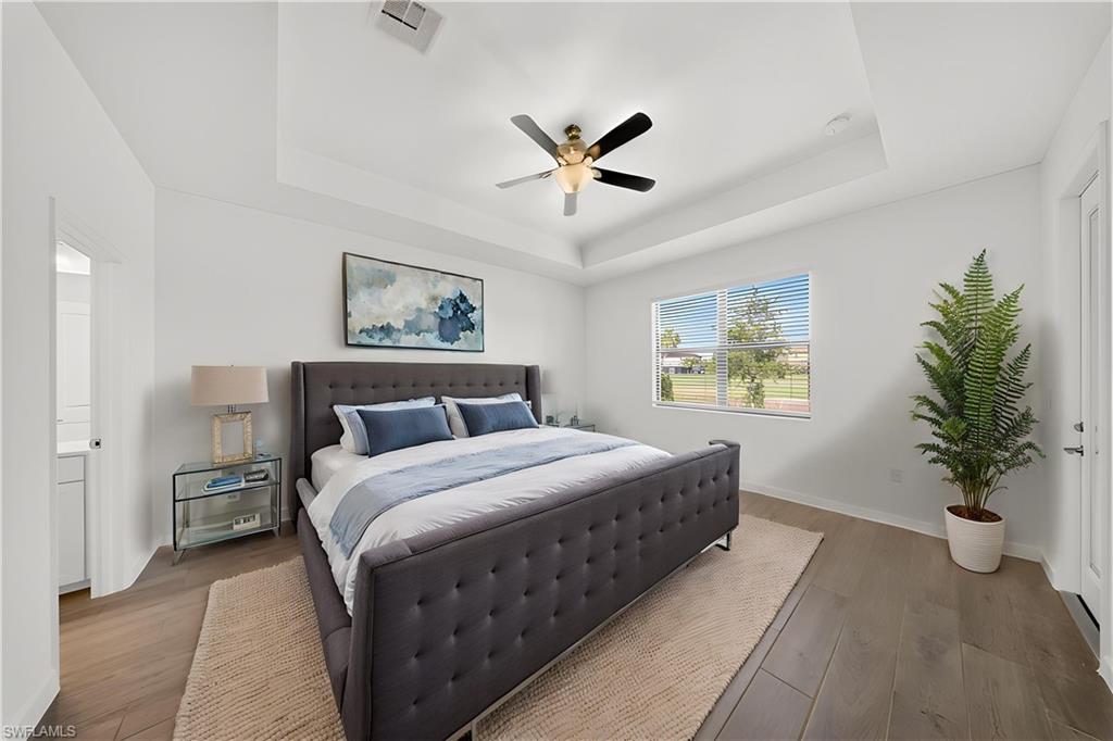Tray ceiling with a ceiling fan, wood-finish flooring, white walls, and a large window with blinds
