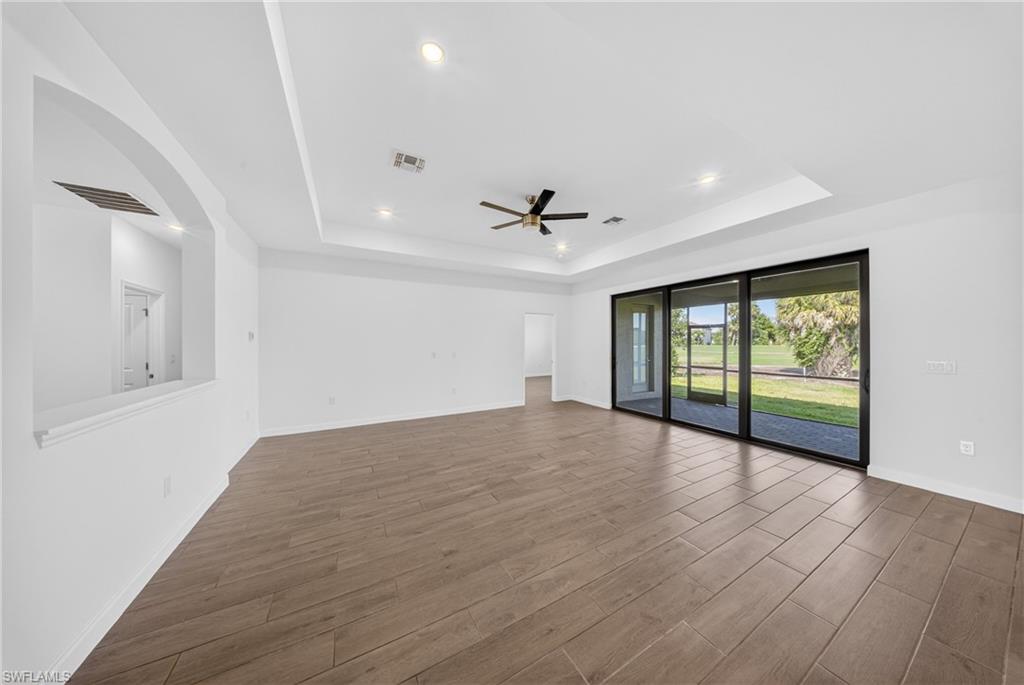 Spacious interior featuring wood-finish flooring, a tray ceiling with recessed lighting and a ceiling fan, and extensive sliding glass doors