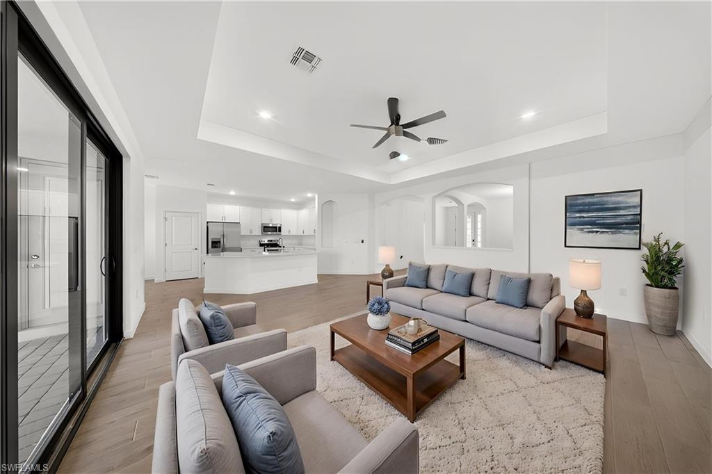 Open-concept living area featuring wood-finish flooring, a tray ceiling with recessed lighting and a ceiling fan, and sliding glass doors