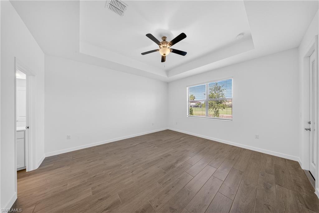 Spacious room featuring wood-finish flooring, a tray ceiling with a ceiling fan, and a large window with horizontal blinds