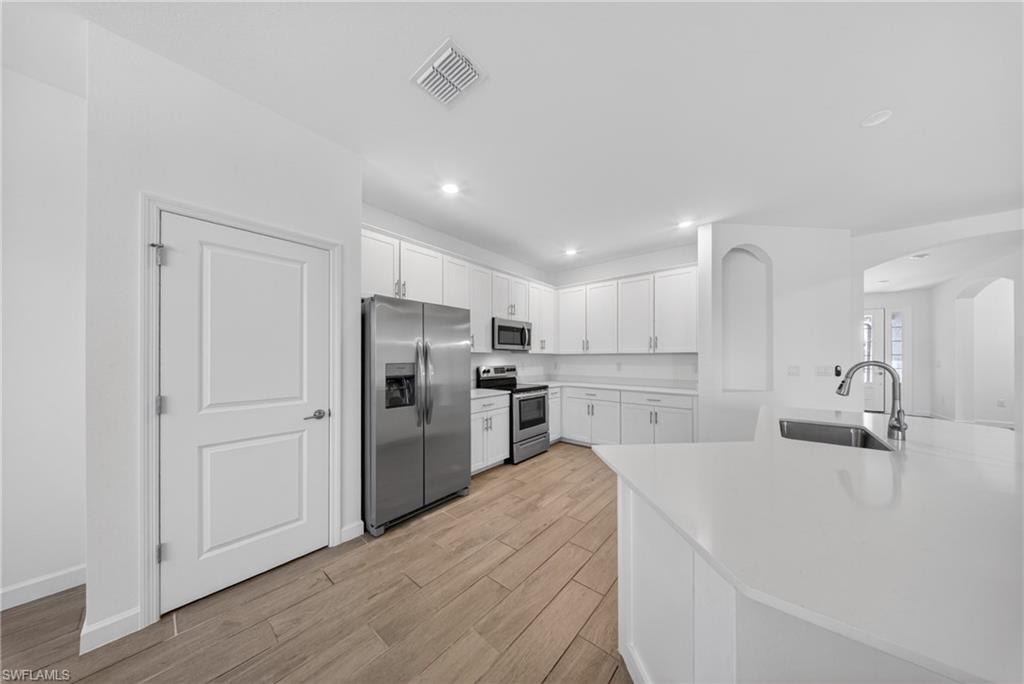 Modern kitchen featuring white cabinetry, stainless steel appliances, and a large central island with an undermount sink