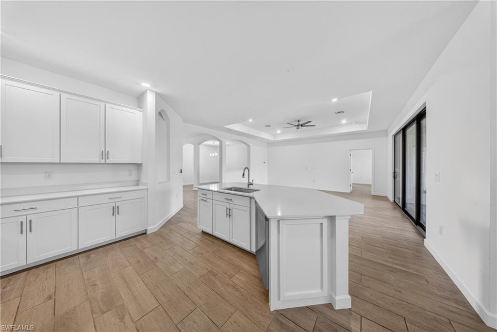 Kitchen featuring an expansive island with a stainless steel sink, white cabinetry, and light-toned countertops