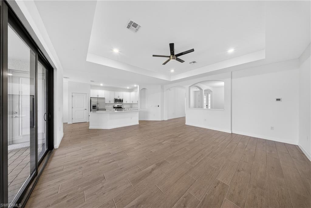Spacious living area featuring wood-finish tile flooring, a tray ceiling with recessed lighting, and a contemporary ceiling fan