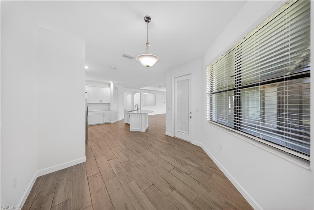 Spacious dining area featuring wood-finish flooring, a large window with horizontal blinds, and a frosted glass panel door