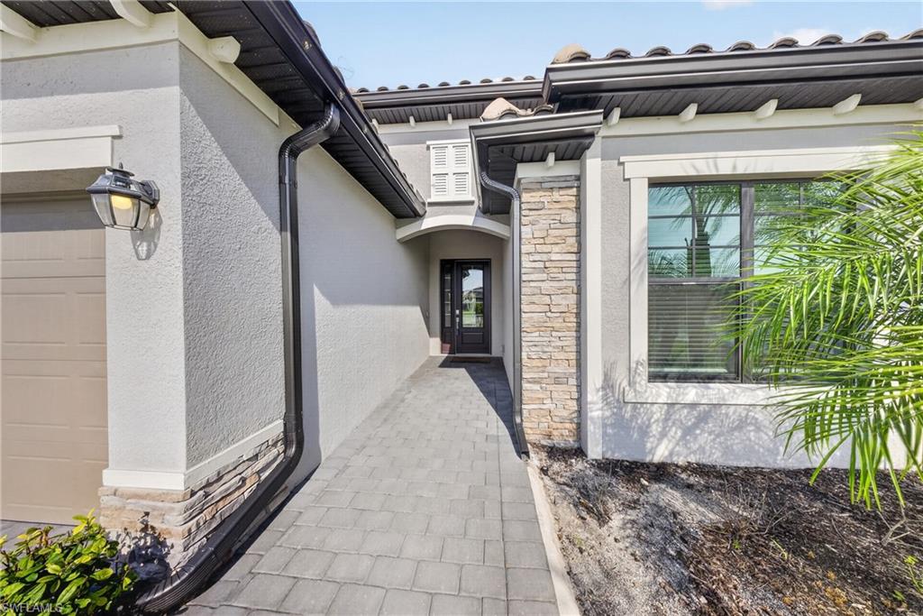 Entryway featuring a paver walkway, stone veneer accents, stucco exterior, and a dark wood-finish front door