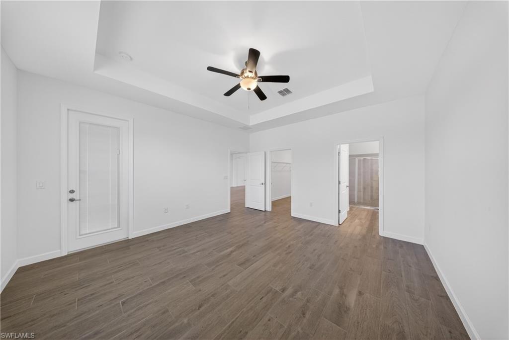 Spacious room featuring wood-finish tile flooring, a tray ceiling, and a ceiling fan with integrated lighting