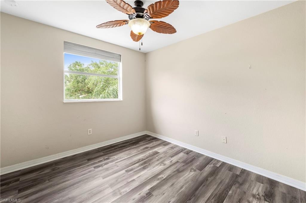 Room featuring wood-finish flooring, a contemporary ceiling fan with leaf-shaped blades, and a window with a green outdoor backdrop