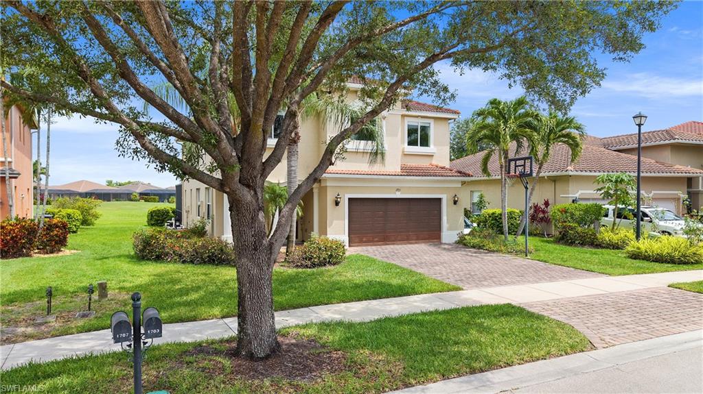 Stucco exterior with a tile roof, featuring a paver driveway, an attached garage, and a lush green lawn