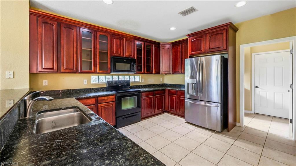Kitchen featuring wood cabinetry, dark countertops, a double basin stainless steel sink, black electric range, and stainless steel refrigerator