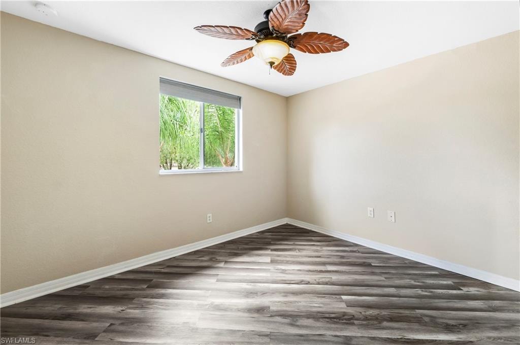 Room featuring wood-finish flooring, a white window frame, and a ceiling fan with leaf-shaped blades