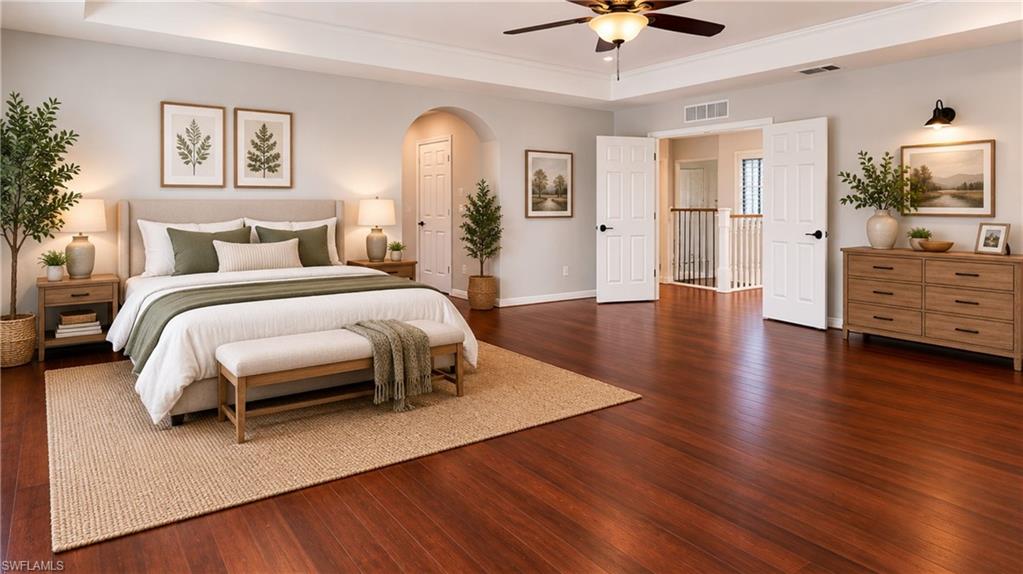 Spacious room featuring wood-finish flooring, a tray ceiling with a ceiling fan, and double doors opening to a hallway with a staircase railing